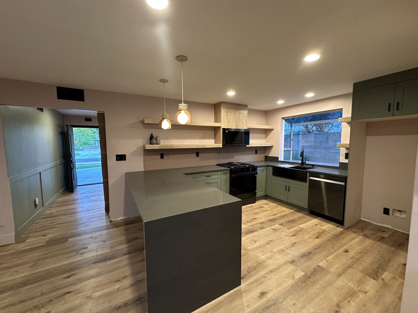 The same kitchen finished with sage-green cabinetry, quartz counters, and floating oak shelves