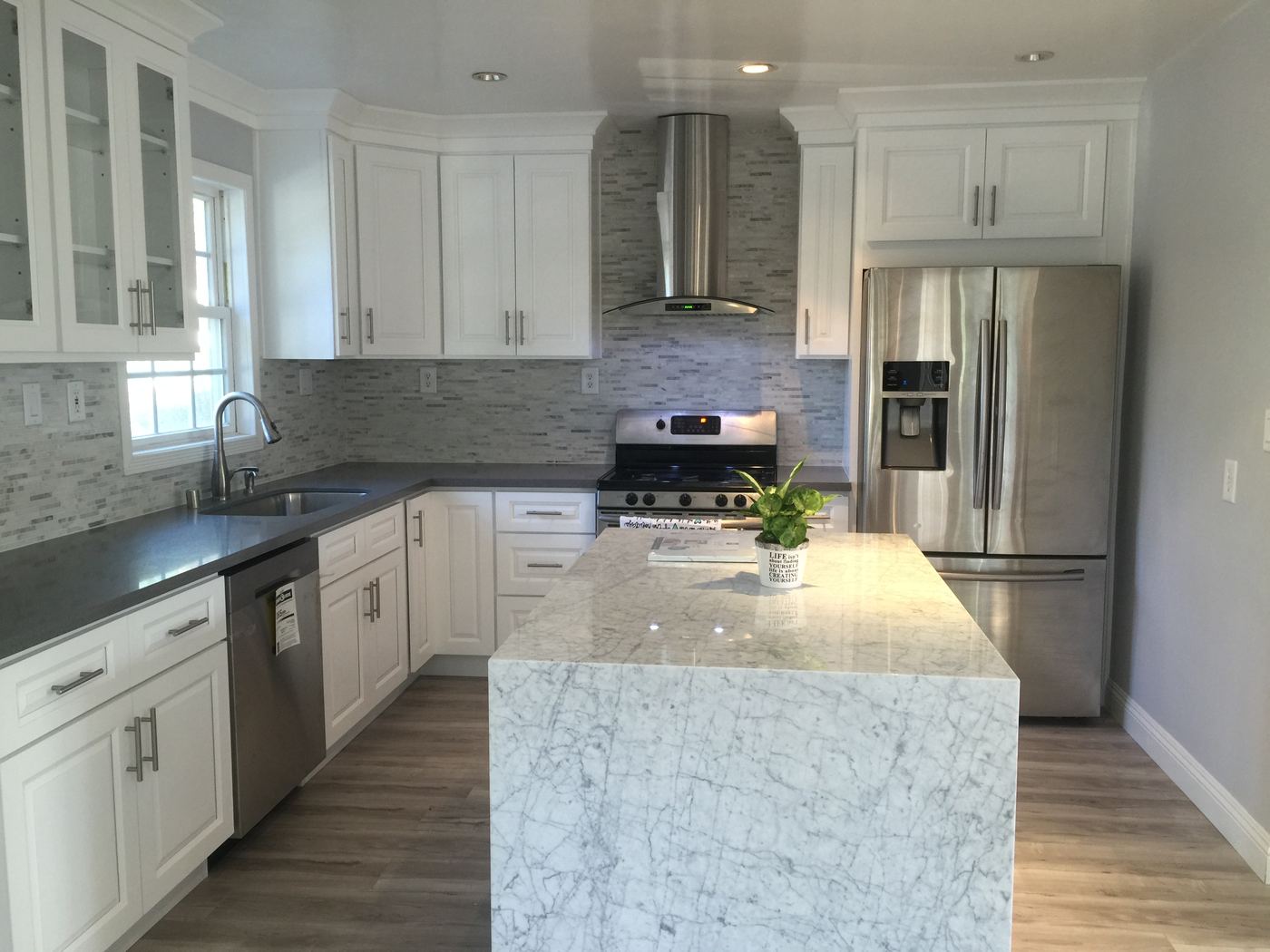 The rebuilt kitchen with white cabinetry, stone backsplash, and a marble waterfall island