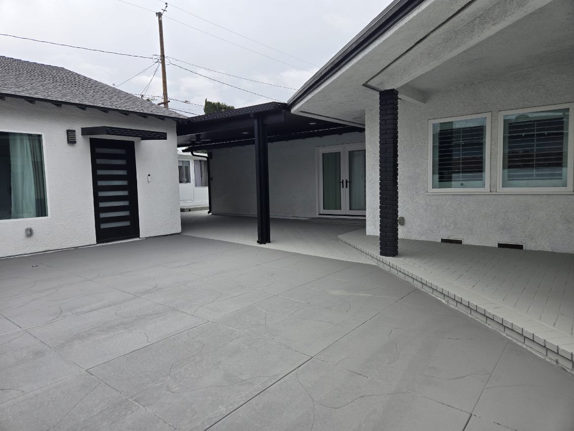 The finished courtyard with stamped hardscaping, a black patio cover, French doors, and refreshed exteriors
