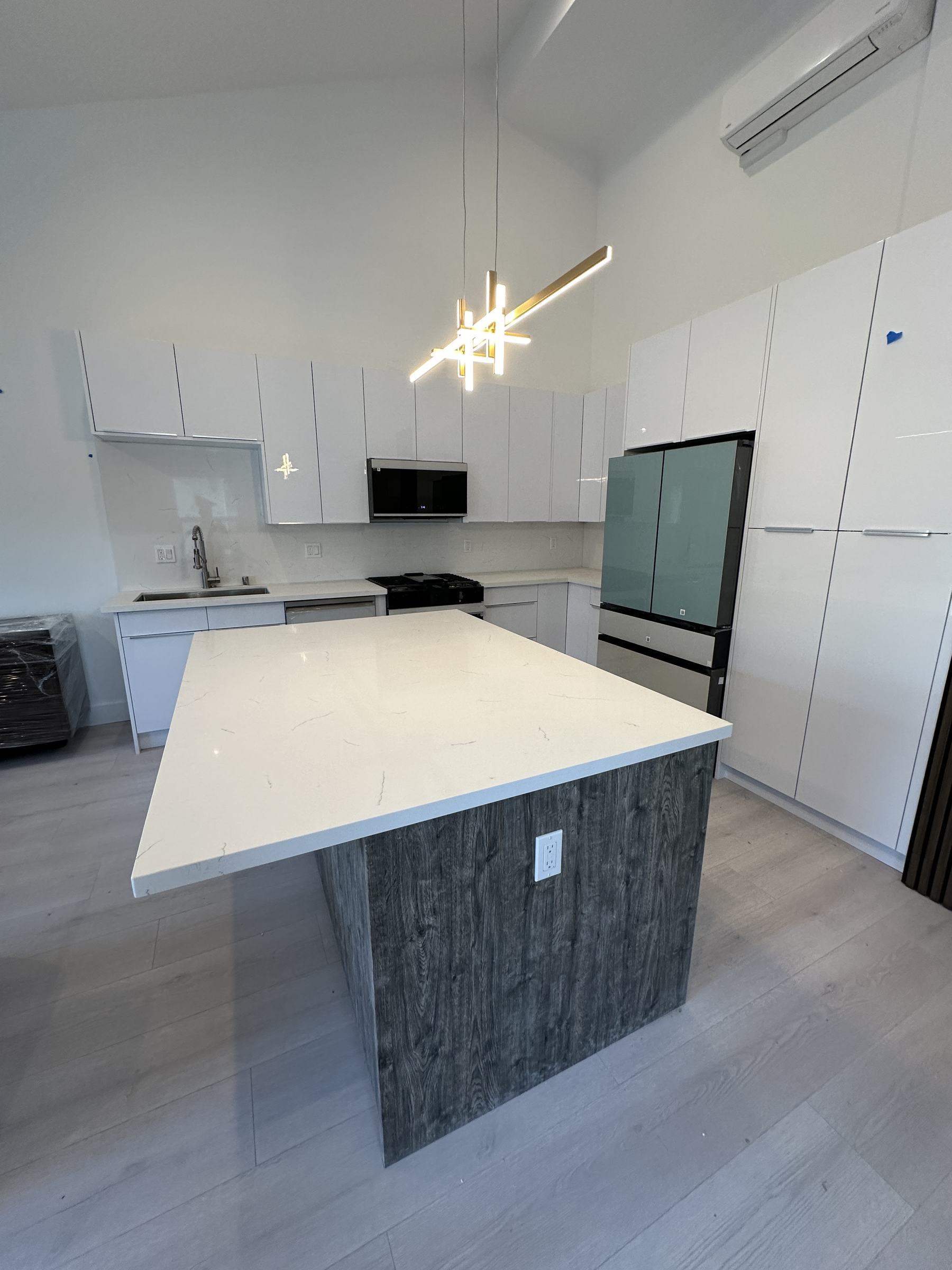 Bright remodeled kitchen with white cabinetry, quartz island, and gold pendant lighting by Angelic Construction