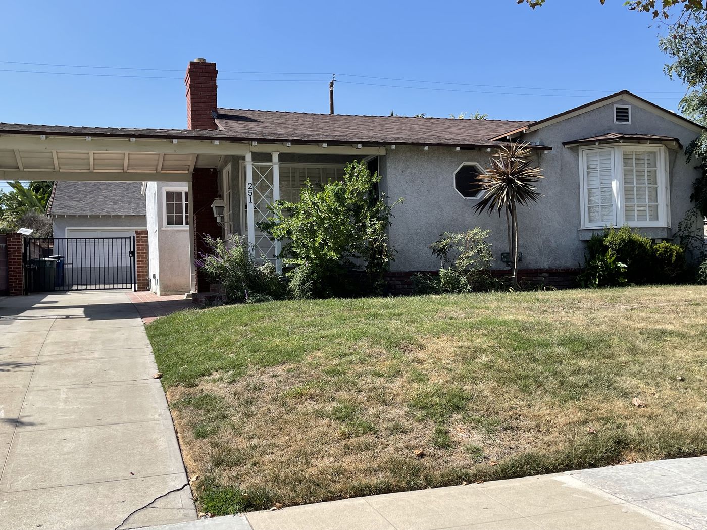 Home exterior with weathered gray stucco, an aging roof, and a dry lawn before its transformation